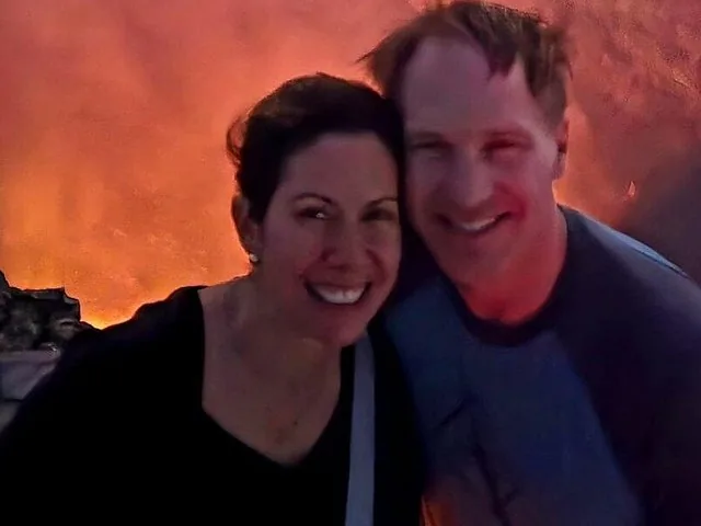 Ein Paar posiert vor einem ausbrechenden Vulkan, der im Hintergrund rot glüht.